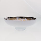 Round white glass fruit bowl on a stand with interior titanium coating and splashes. Mirror effect design glass bowl.